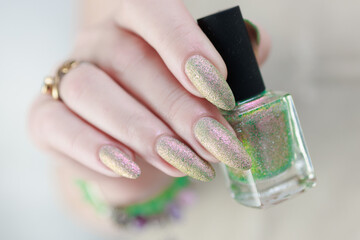 Female hand with long nails and a nude beige and green manicure holds a bottle of nail polish