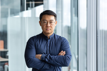Portrait of successful and serious asian boss in shirt, man looking at camera with crossed arms...