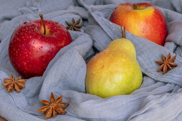 A pear and two red apples wetted with water drops are wrapped in a gray scarf with star anise