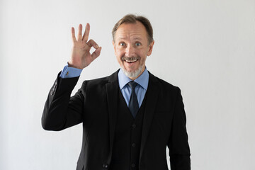 Portrait of successful mature businessman showing ok gesture. Happy senior Caucasian man wearing three piece suit looking at camera and smiling. Successful businessman concept