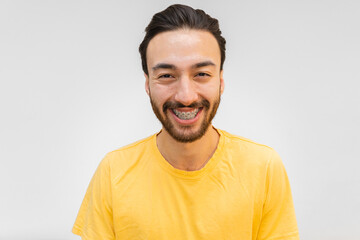 Obraz premium Young latin and hispanic man with beard and braces smiling looking at camera with a yellow t-shirt. White background.