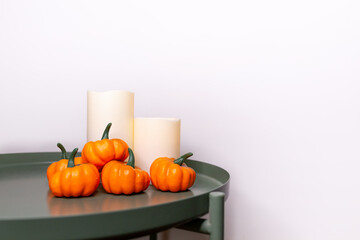 minimalistic autumn home decor for halloween, seasonal decorations, pumpkins, harvest, thanksgiving day, all saints day, scandinavian interior, candles, table, white wall, space for text, postcard