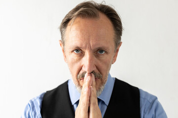 Close-up of serious mature businessman praying. Portrait of senior Caucasian manager wearing formalwear looking at camera and pleading against white background. Hope and faith concept