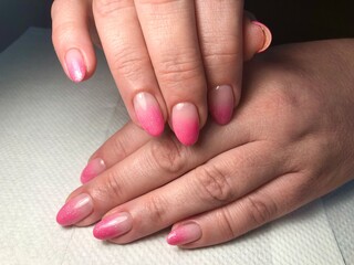 A close-up of a woman’s hands with pink gradient nails. The nails have a soft ombre effect, transitioning from light to dark pink. A simple yet elegant manicure on natural-length nails. © Yana Perelotova