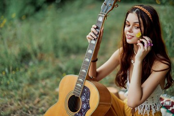 Happy hippie woman with a guitar relaxing in nature sitting on a plaid smiling and enjoying the...