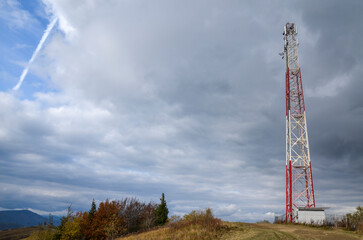 Telecommunication and cell phone tower on top of a hill with mountains on background 