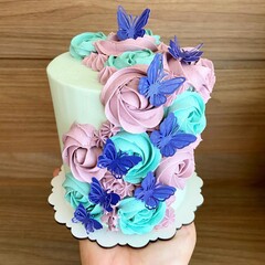 Hand holding cake decorated with flowers made of icing, pink and green and butterflies. Front view.