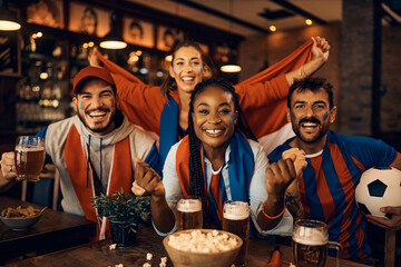 Happy soccer fans cheering while watching game on TV in pub.