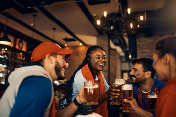 Happy soccer fans celebrating their team's victory and toasting with beer in pub.