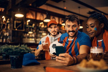 Group of soccer fans watching match results on smart phone during world cup in pub.