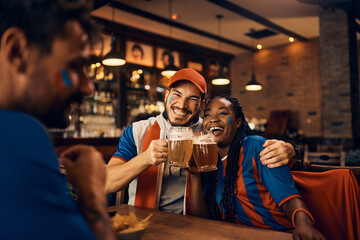 Cheerful couple of soccer fans has fun while drinking beer in pub.
