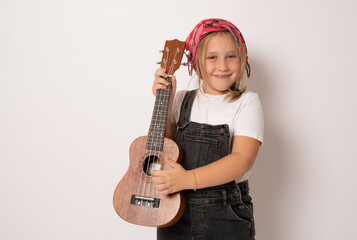Cute little girl in denim clothing playing ukulele over white background. Happy vacation concept.