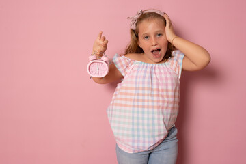 Children concept. A girl holds an alarm clock in her hands, plays with it, looks at the camera. Isolated over white background.