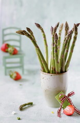 Composition with green fresh asparagus and strawberries on a green pastel background, culinary magazine / book, culinary / food photography, healthy eating concept, vegan, vegetarian diet.