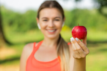 A young woman in a pink top holds a red apple in the open air. Concept of healthy eating