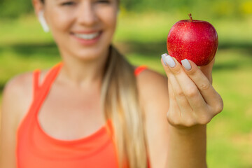 A young woman in a pink top holds a red apple in the open air. Concept of healthy eating