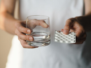 Woman holding a blister pack of pills and glass of water. Female going to take tablet from...