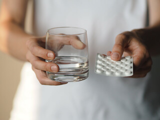Woman holding a blister pack of pills and glass of water. Female going to take tablet from headache, painkiller, medication drinking water from glass. Medicine, health care and people concept.
