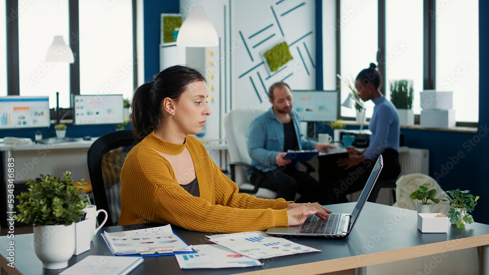 Poster focused startup employee typing using laptop keyboard while looking at screen and smiling sitting at