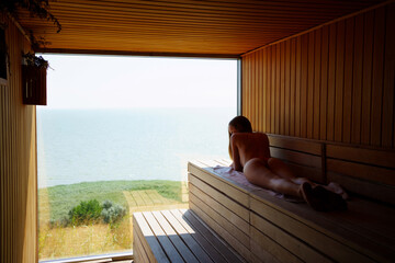 woman topless lies on a bench in the sauna with the panoramic window. 