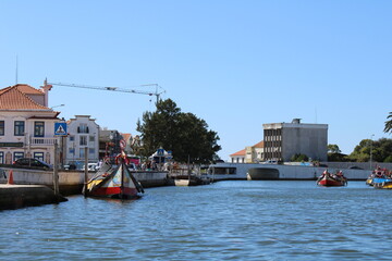 Fototapeta na wymiar Aveiro, Portugal. 2022 September 25. Traditional boats in the Ria of Aveiro, Portugal. Colorful Moliceiro boat rides in Aveiro with tourists. Big buildings around the river and colorful bridges.