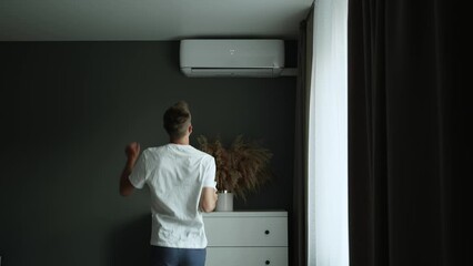 Happy man turns on air conditioner and rejoices in cool air.