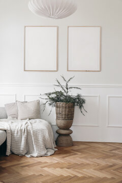 Christmas interior. Two blank vertical wooden picture frames mockups. White wall background.. Bed, sofa with linen cushions, blanket. Larch, pine tree branches in wicker basket, wooden coffee table.