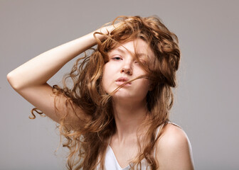 portrait of a beautiful woman holding long curly hair with her hand looking at the camera