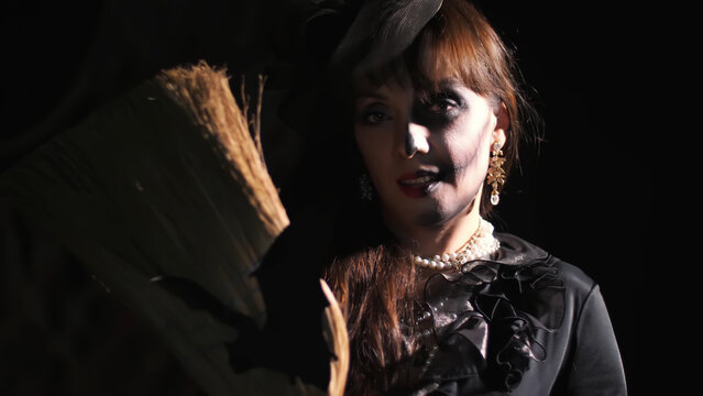 Halloween party, night, frightening portrait of a woman in the twilight, in the rays of light. woman with a terrible make-up in a black witch costume. she holds a broom with a bat. High quality photo