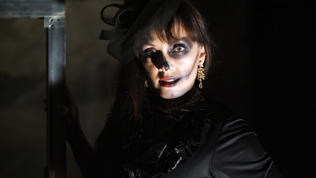 Halloween party, night, frightening portrait of a woman in the twilight, in the rays of light. woman with a terrible make-up in a black witch costume. High quality photo