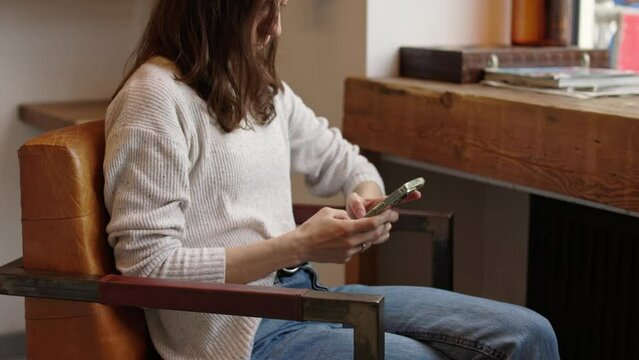 Unrecognizable business woman sitting in armchair at wooden desk and typing on cellphone answering email in coffeeshop during break with free wifi 4k