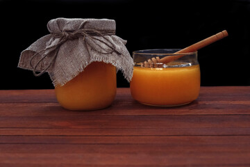 Honey in a glass jar with a spoon with a film effect, grain, noise out of focus on a brown wooden table with an empty space for text, close-up, dessert concept, healthy nutrition, health and immunity