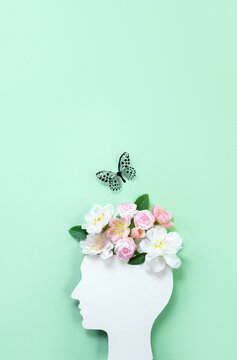 Cardboard silhouette of human head decorated with flowers and butterfly on mint background. World mental health day concept. Vertical banner. Copy space