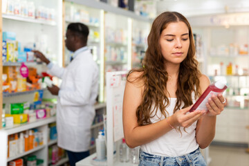 Young woman who came to the pharmacy attentive chooses a hair care remedy, studying its components