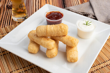 Tequeño sandwiches of dough and cheese with white sauce and red sauce on square white plate on wooden table
