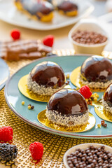  round cake with raspberry set on a blue plate and chocolate decor on a beige table on a light background.Berry dessert.Delicate airy cake souffle.Appetizing cupcakes and pastries.