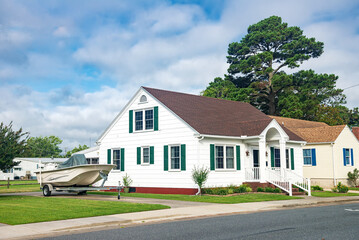 Cute brightly painted white shingled cottage with a boat in the parking lot. coastal town on a sunny day.