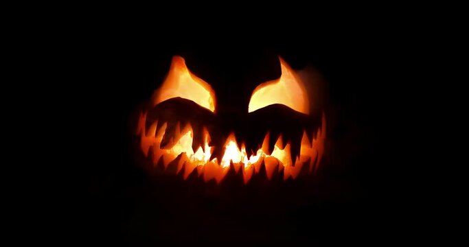 Spooky Halloween jack o lantern with scary face carved out of a pumpkin glowing with flickering light and emitting smoke.