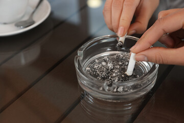 Women putting out cigarettes in ashtray at table, closeup