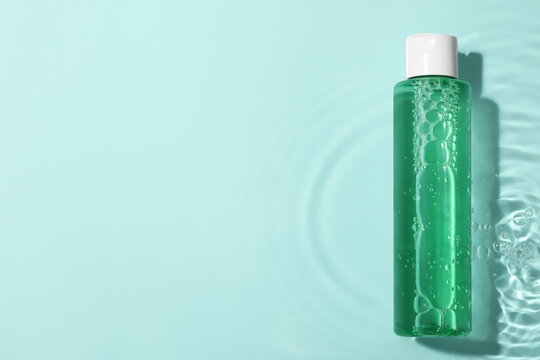 Wet bottle of micellar water and petals on light blue background, top view. Space for text
