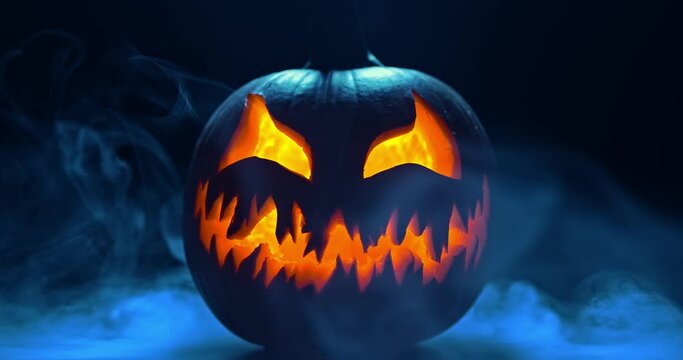 Spooky Halloween jack o lantern with glowing scary face carved out of a pumpkin and surrounded by smoke and mist.
