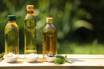 Different cooking oils and ingredients on wooden table against blurred green background. Space for text