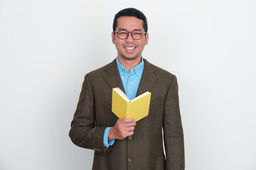Asian businessman wearing suit smiling while holding a book - obrazy, fototapety, plakaty