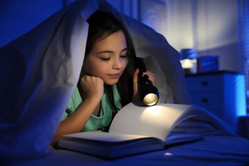 Little girl with flashlight reading fairy tale in dark bedroom - obrazy, fototapety, plakaty