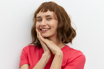 Fototapeta premium horizontal photo of a cute, attractive, laughing red-haired woman in a red cotton T-shirt standing on a white background and holding her hands near her face.