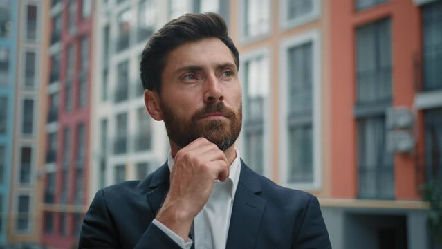 Caucasian smart puzzled thoughtful man hold hand to chin dreaming about career growth successful employer in stylish black suit stand outside modern office pondering idea planning business development