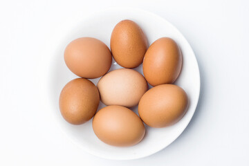seven chicken eggs in a white bowl on white background