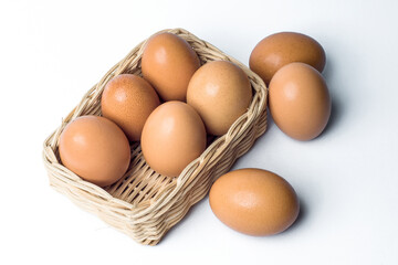 Five chicken eggs in a rattan basket and three eggs outside on white background