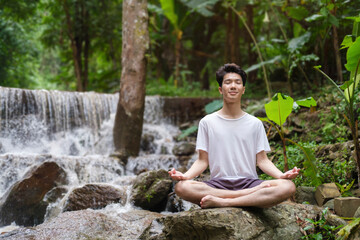 Full body young male in casual clothes sitting on stone edge in lotus pose. Sport, yoga, pilates, fitness, healthy lifestyle concept.