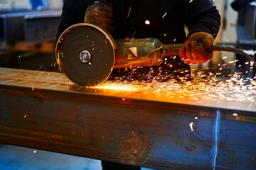 Worker cuts metal beam with abrasive disk in plant workshop